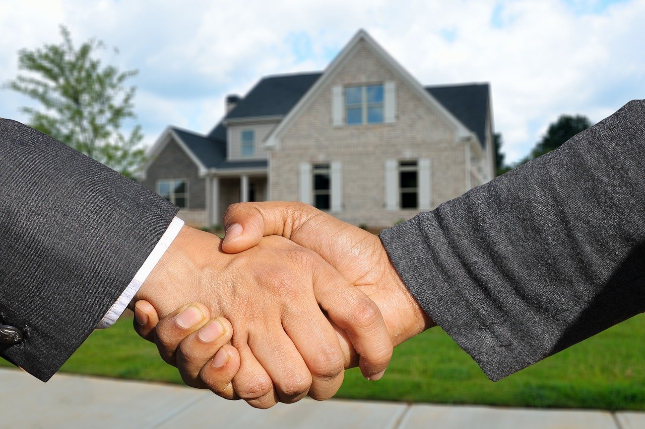 Two business professionals shake hands in front of a house, symbolizing successful real estate lead conversion.