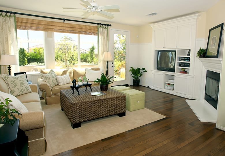 Bright living room with beige furniture, wooden floors, decorative plants, and a media unit, featuring large windows and natural light.
