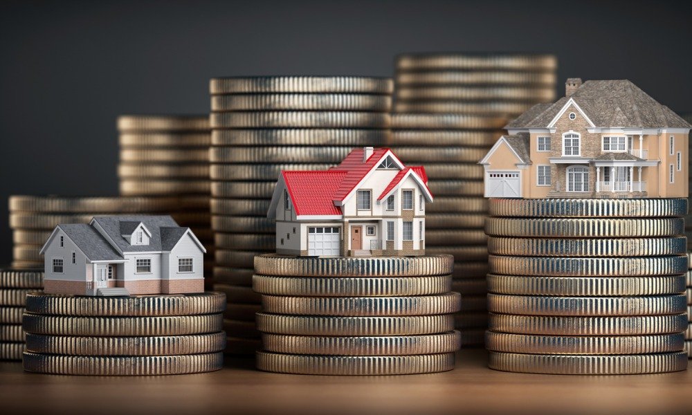 Three miniature houses sit atop stacks of coins, symbolizing real estate value and investment in a financial context.