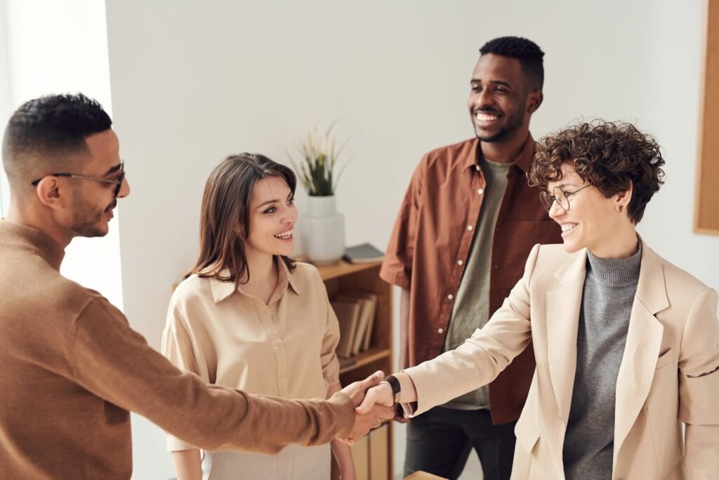 A group of four individuals engaged in a handshake, symbolizing agreement or collaboration, in a modern office setting.