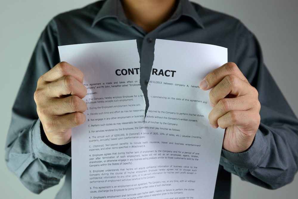 A person tears a contract, symbolizing the termination of an agreement, with the word "CONTRACT" prominently visible on the page.