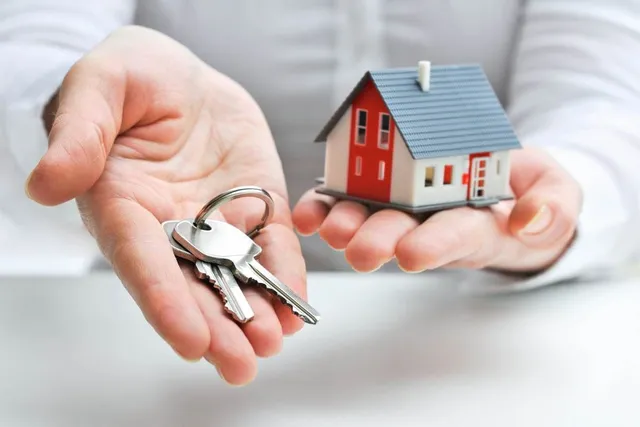 A person holds a set of keys in one hand and a small model house in the other, symbolizing homeownership and new beginnings.
