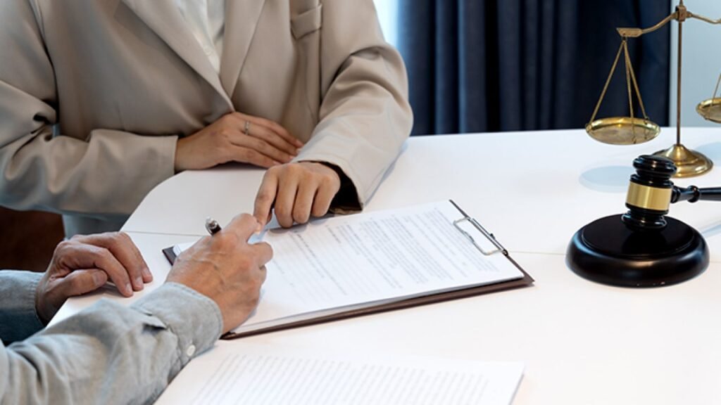Two people discussing a legal document at a table, with a gavel and scales of justice in view, indicating a legal consultation.
