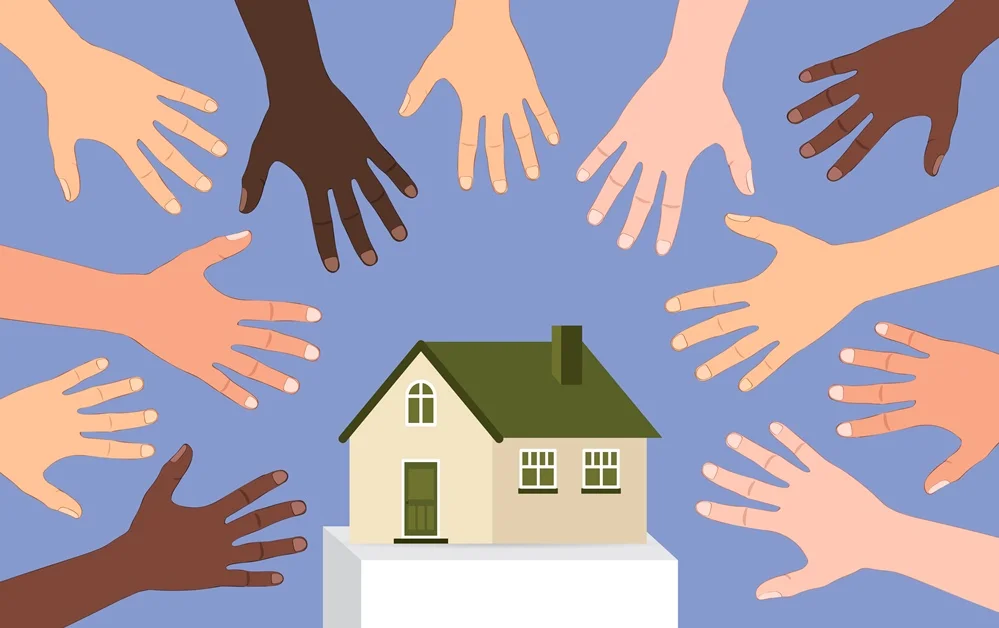 Diverse hands reach out towards a small house, symbolizing community support and collaboration in housing initiatives.