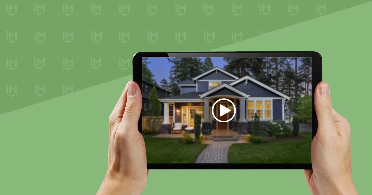 A hand holds a tablet displaying a video preview of a charming blue house surrounded by lush greenery and a welcoming pathway.