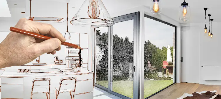 Hand sketching a modern kitchen with a view of a garden through large glass doors, blending design and reality.