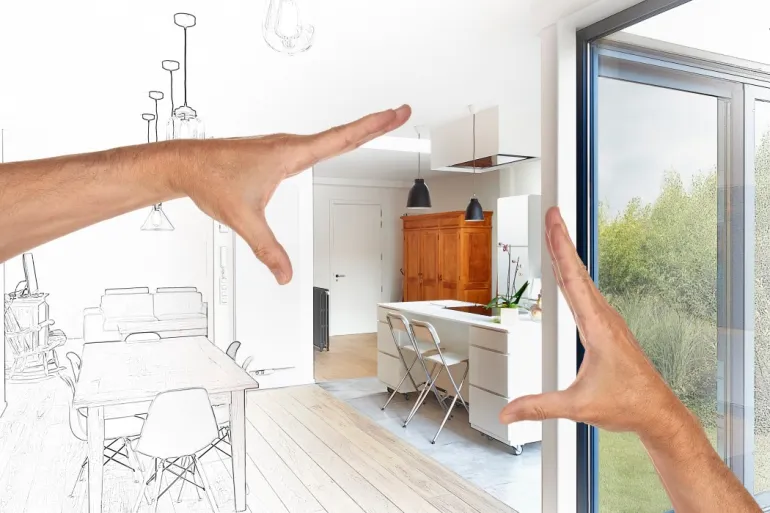 A person's hands gesture towards a modern kitchen, blending a sketched layout with a real-life interior view.
