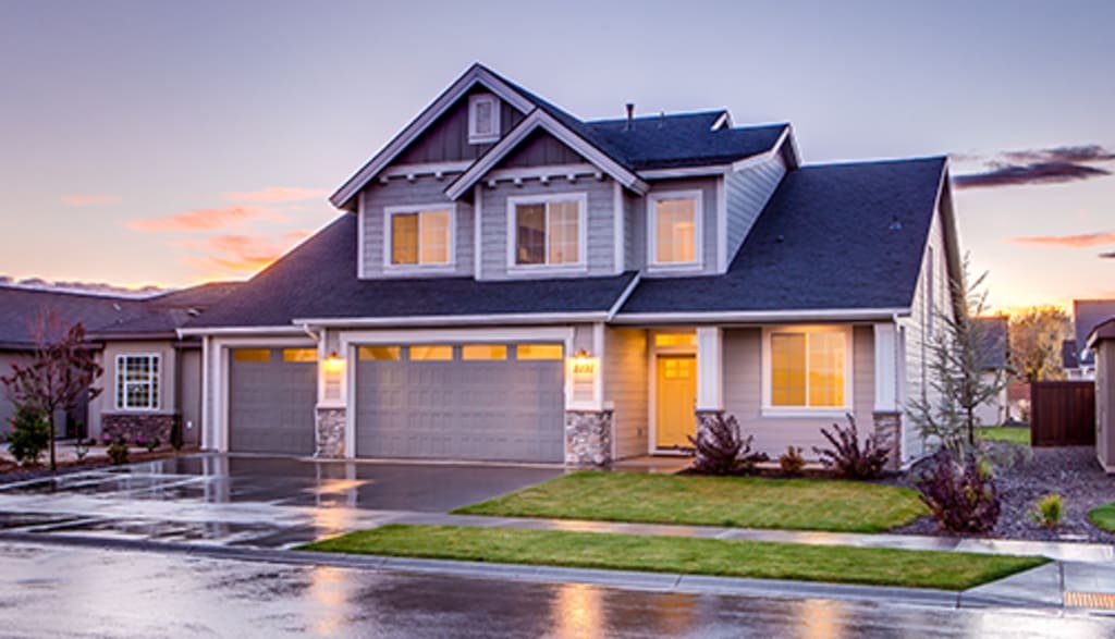 A modern two-story house with a gray facade, large windows, and a manicured lawn, captured during a colorful sunset.