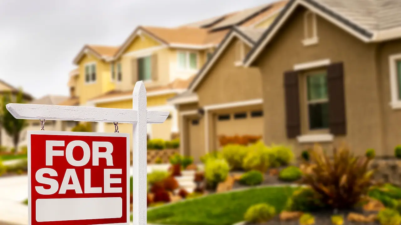A "For Sale" sign stands in front of well-kept homes with manicured lawns, indicating real estate opportunities in the area.