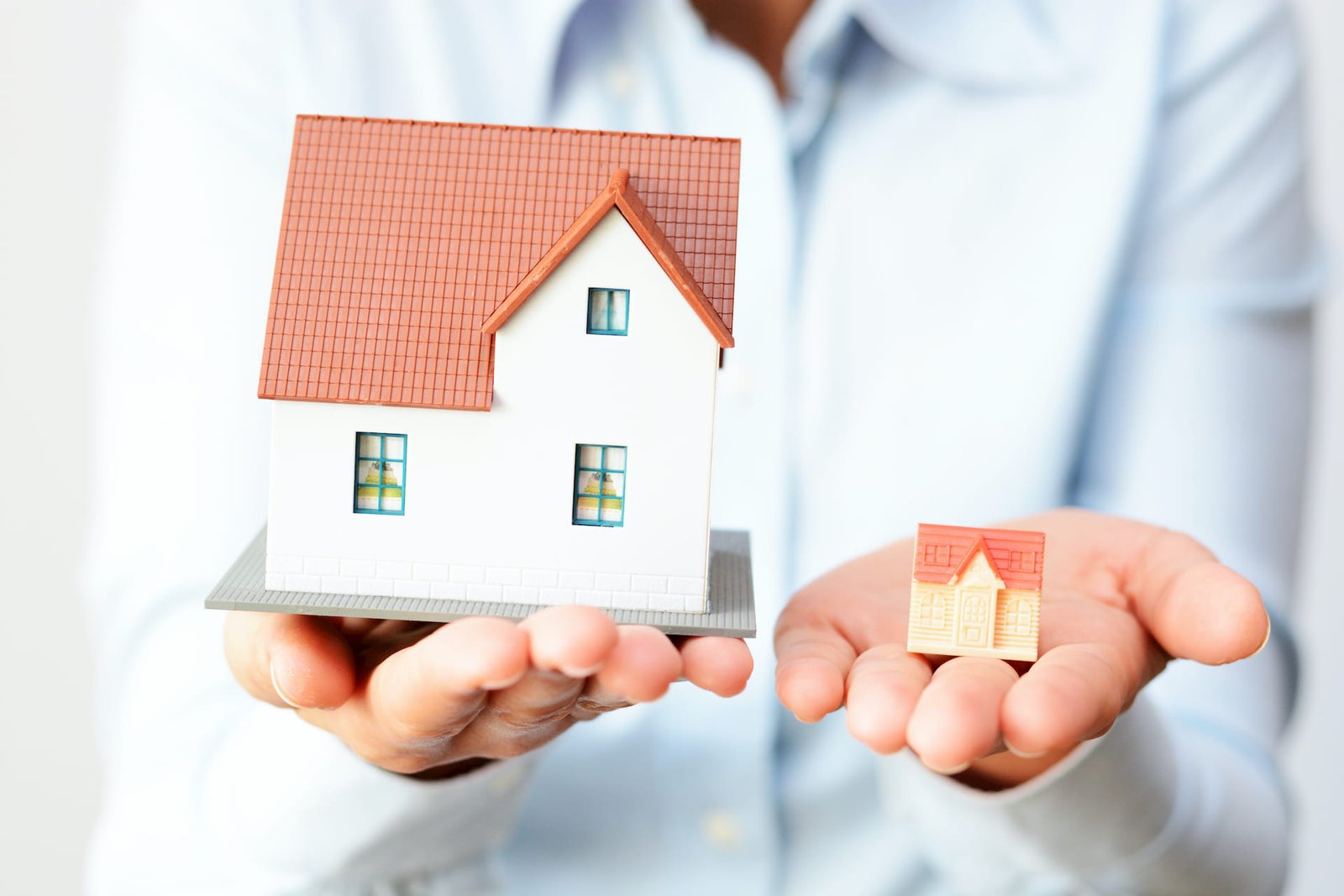 A person holds a large model house in one hand and a smaller house model in the other, symbolizing real estate and property.