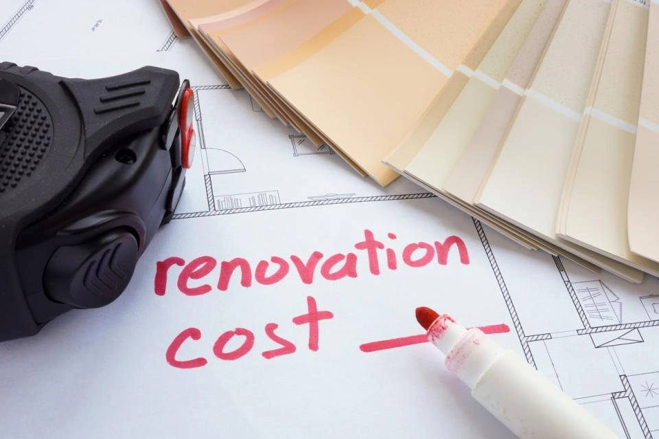 A tape measure and red marker lie on a renovation blueprint beside color palettes, highlighting a focus on renovation costs.