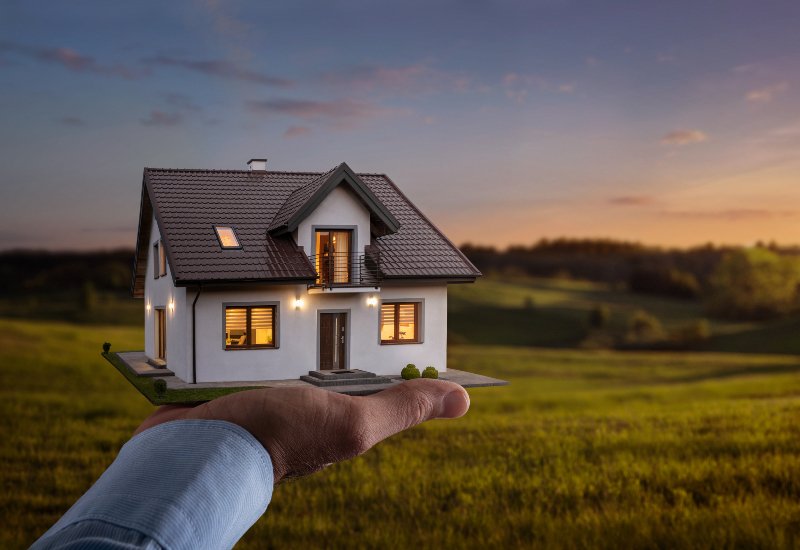 Male hand showing, offering a new dream house at the empty field with copy space
