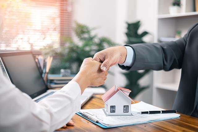 A real estate agent shakes hands with a client over a model house and paperwork, symbolizing a successful property agreement.