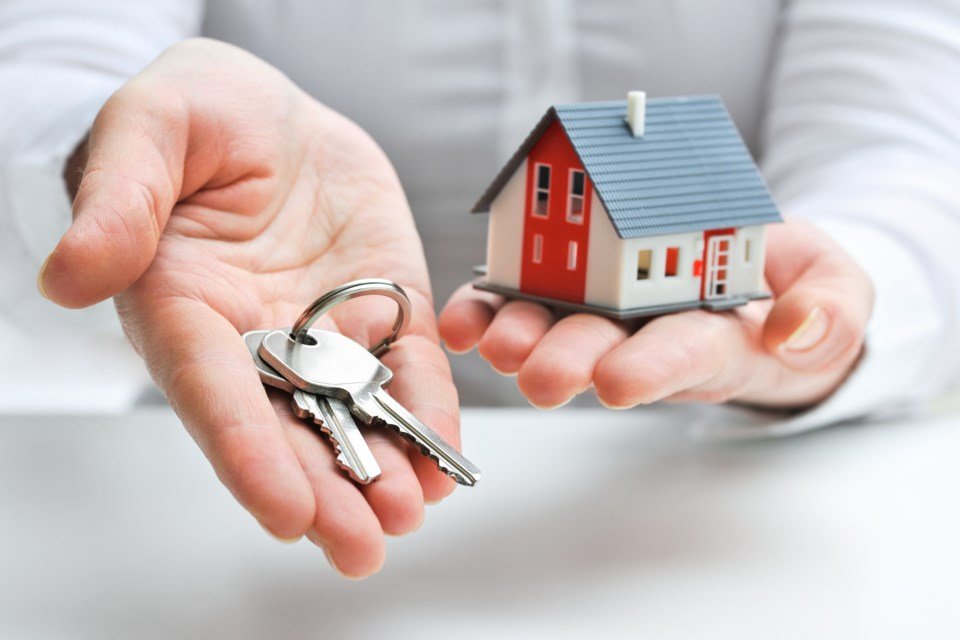 A person holds a model house in one hand and a set of keys in the other, symbolizing home ownership and new beginnings.